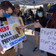 Two protesting Activision Blizzard employees wearing face masks and holding white signs that say "Nerf Male Privilege" and "Fight Bad Guys In Game, Fight Bad Guys IRL."